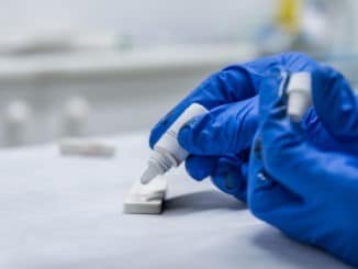 Close-up of hands of a nurse with individual protection equipment, in the process of blood collection to make a rapid test for covid-19(coronavirus), in a hospital ward with sanitary elements in the background.