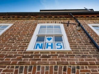 Vertical view of a home-made Love NHS sign seen attached to a sash window for a town house.