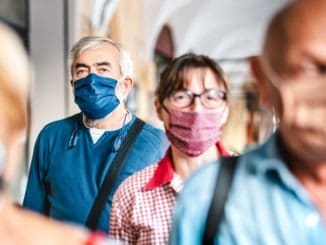 Crowd of adult citizens walking on city street – New reality lifestyle concept with senior people with covered faces – Selective focus on bearded man with blue protective mask
