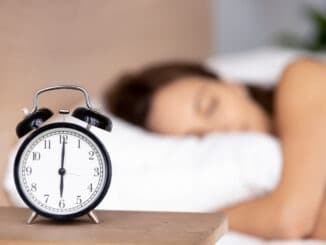 Alarm clock on bedside table with woman sleeping on background