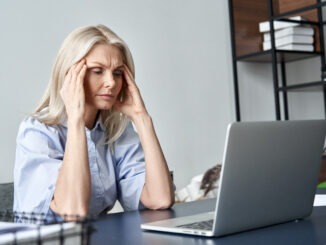 Stressed forgetful old middle aged business woman suffering from headache after computer work. Tired upset 50s lady massaging head feeling stress, fatigue or migraine using laptop at home office.