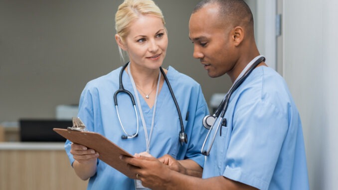 Medical multiethnic staff having discussion in a hospital hallway. Male and female nurse wearing blue scrubs working in a medical clinic. Two hospital workers discussing on laboratory test.