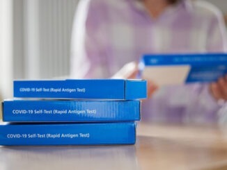 Close Up Of Woman At Home Reading Instructions On Supply Of Covid-19 Rapid Antigen Self-Testing Kits