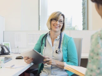 Happy mature female doctor with digital tablet looking at nurse while sitting at desk