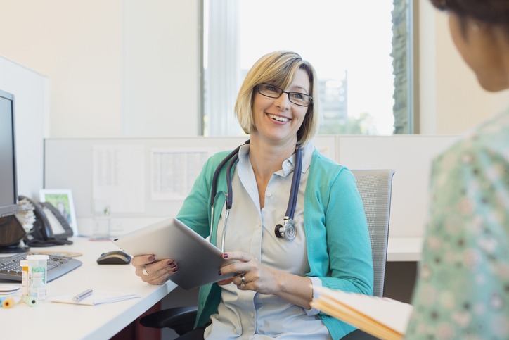Happy mature female doctor with digital tablet looking at nurse while sitting at desk