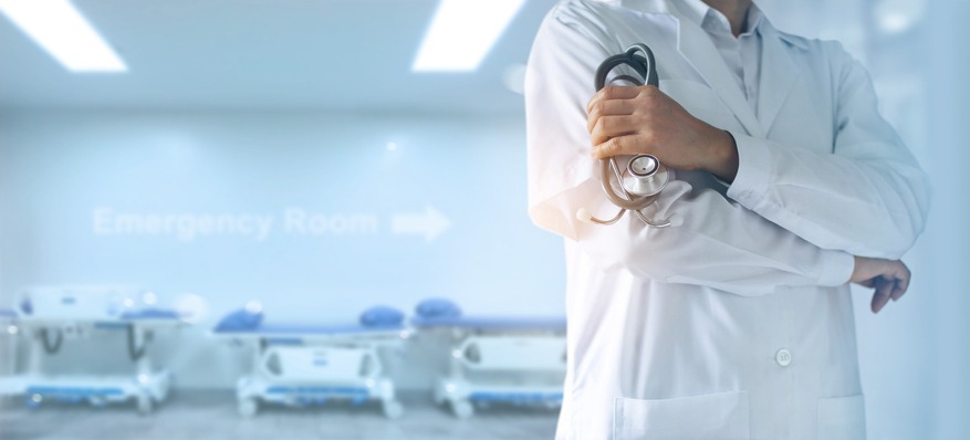 Medicine doctor with stethoscope in hand, confidently standing in front of emergency room, patient beds behind him, hospital background