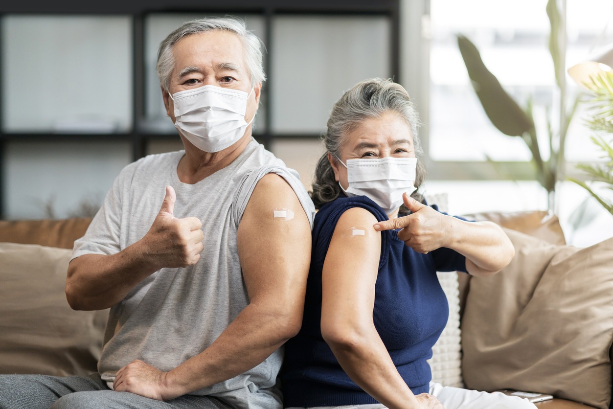 old asian senior couple wearing face mask virus protection happiness cheerful show bandage injection covid-19 vaccinated with hand gesture point and confident for virus protection