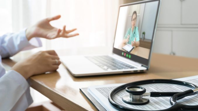 Asian doctor and nurse team making video call for discussing, consulting for pandemic virus together via internet and wireless technology with laptop computer on wood table in meeting at medical room of hospital.