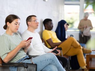 Relaxed young girl browsing websites on smartphone while sitting in lobby of job center or employment office, waiting for appointment