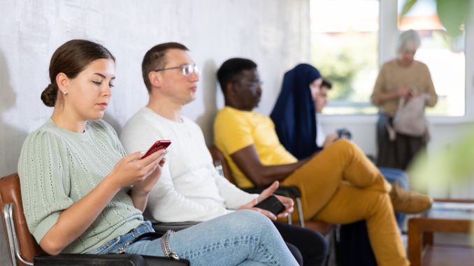 Relaxed young girl browsing websites on smartphone while sitting in lobby of job center or employment office, waiting for appointment