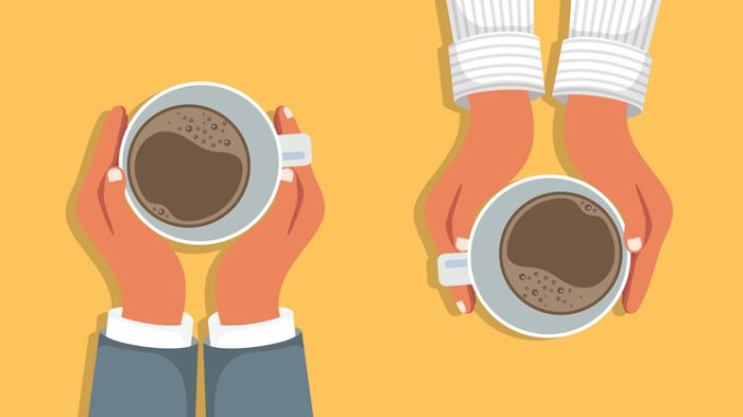 Hands holding cups of coffee on table background.