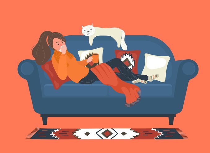 Flu. Ill woman lays on sofa at home and blowing her nose.