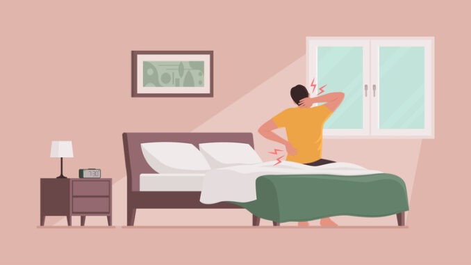 Man waking up and suffering from back pain, he is sitting on the bed and touching his neck and lower back