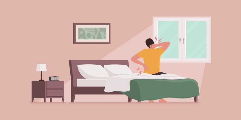 Man waking up and suffering from back pain, he is sitting on the bed and touching his neck and lower back