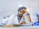 Overworked doctor in his office. Tired male scientist trying to focus, rubbing his forehead with fingers. Mid adult male doctor working long hours. Stressed male doctor sat at his desk
