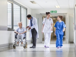Doctors & nurse in hospital corridor with senior female patient in wheel chair with male Asian doctor