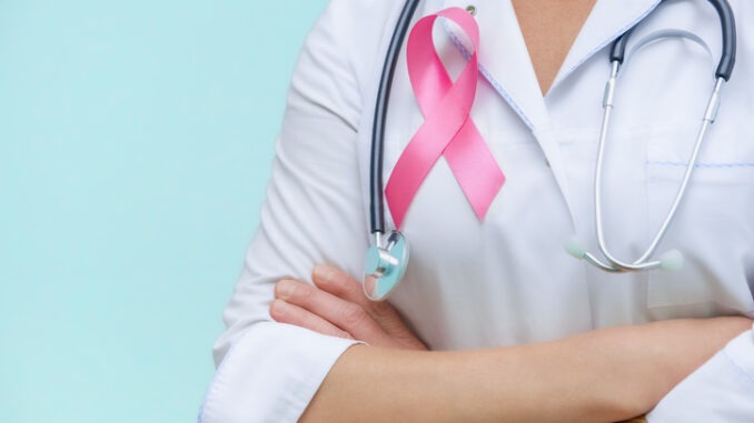 Doctor with folded arms and a stethoscope on his neck, shows a pink ribbon close-up on uniform on a blue background.