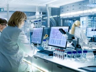 Female and Male Scientists Working on their Computers In Big Modern Laboratory. Various Shelves with Beakers, Chemicals and Different Technical Equipment is Visible.