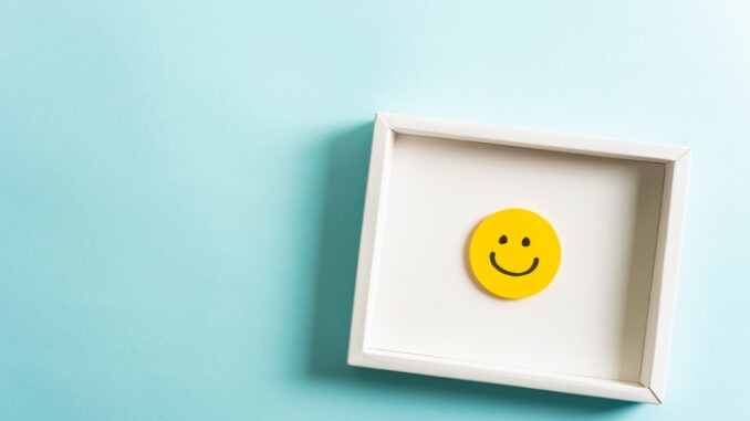 Concept of well-being, well done, feedback, employee recognition award. Happy yellow smiling emoticon face frame hanging on blue background with empty space for text.