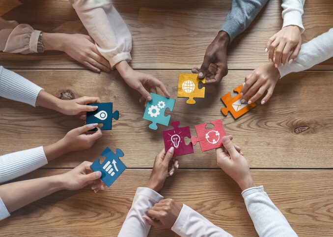 International team of coworkers sitting around table, putting colorful puzzles together, teamwork concept, top view