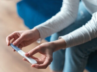Cropped view of woman hands with domestic pregnancy test being at home. Process of waiting for test results when sitting on sofa. Motherhood concept