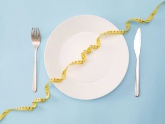 Healthy Eating Concept: White Plate with Measuring yellow Tape, Fork and Knife on a Blue Background