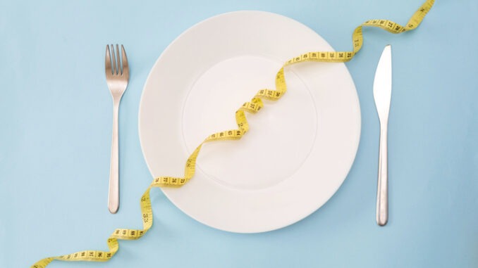 Healthy Eating Concept: White Plate with Measuring yellow Tape, Fork and Knife on a Blue Background