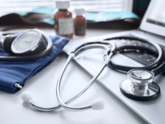 Stethoscope on laptop keyboard in doctor surgery with sphygmomanometer blood pressure monitor and pills