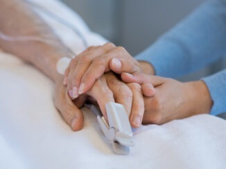 Daughter holding the hand of an elderly father. Closeup of woman holding senior man hand in hospital. Close up of nurse holding old man hand with oxygen saturated probe on finger.