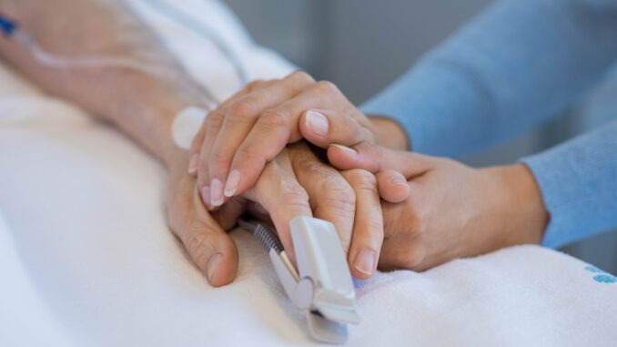 Daughter holding the hand of an elderly father. Closeup of woman holding senior man hand in hospital. Close up of nurse holding old man hand with oxygen saturated probe on finger.