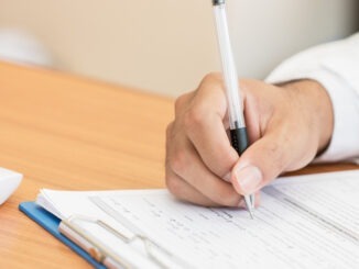 Healthcare medical Expenses concept, Hands Doctor's writing and working on prescription clipboard with record information paper folders on desk in hospital or clinic. Selective focus