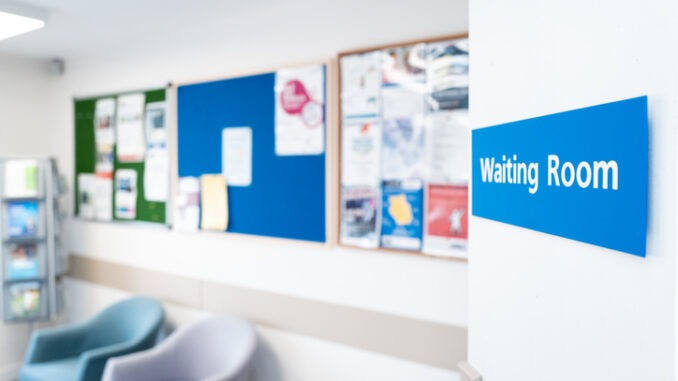 Shallow focus of a typical NHS hospital waiting room sign seen in a British hospital. Seating and information material can be seen in the room.