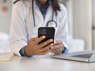 Close up female doctor using smartphone at workplace, access records, review medical histories, conduct virtual consultations with patients, provide advice, prescribe medication through telehealth app