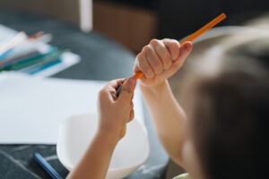 Child Hands Sharpening Pencil Into Plastic Sharpener Cup, Closeup Of Precise Grip And Shavings, Desk Setting